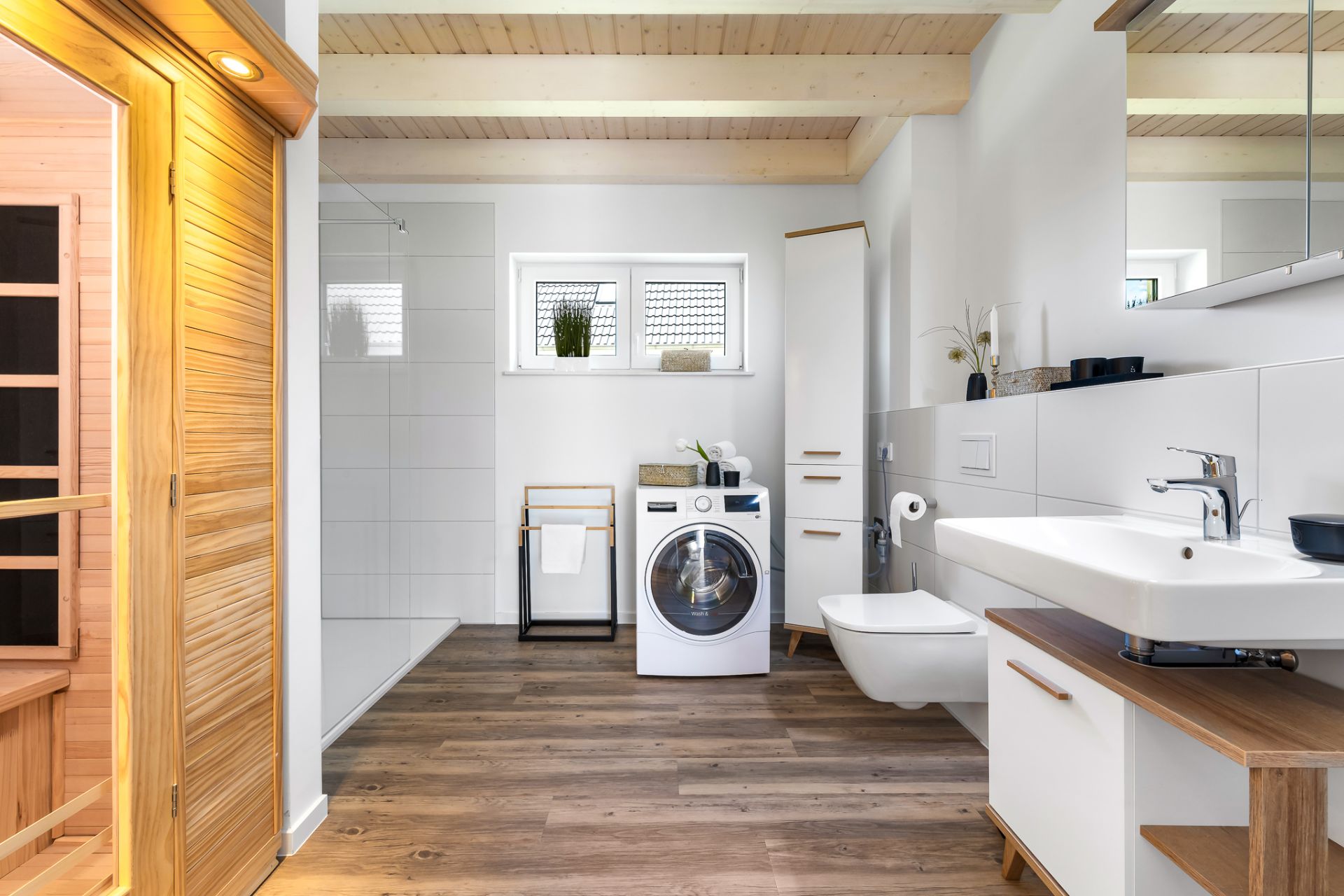 Modernes Badezimmer mit Sauna, Waschmaschine, weißem Waschbecken und Holzfußboden.