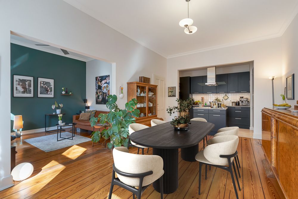 Helles Esszimmer mit rundem Tisch, sechs Stühlen, offener Küche und Wohnbereich mit Pflanzen.