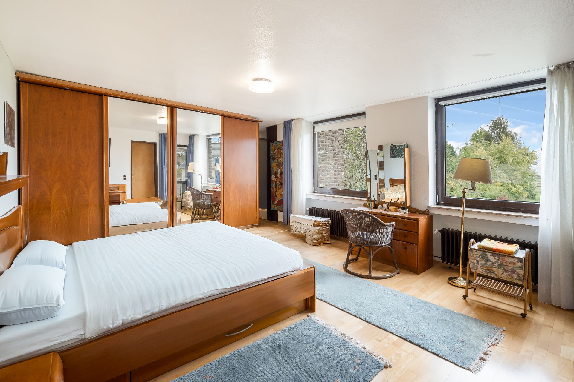 Helles Schlafzimmer mit großem Bett, Spiegelschrank, Schreibtisch und großen Fenstern mit Ausblick.