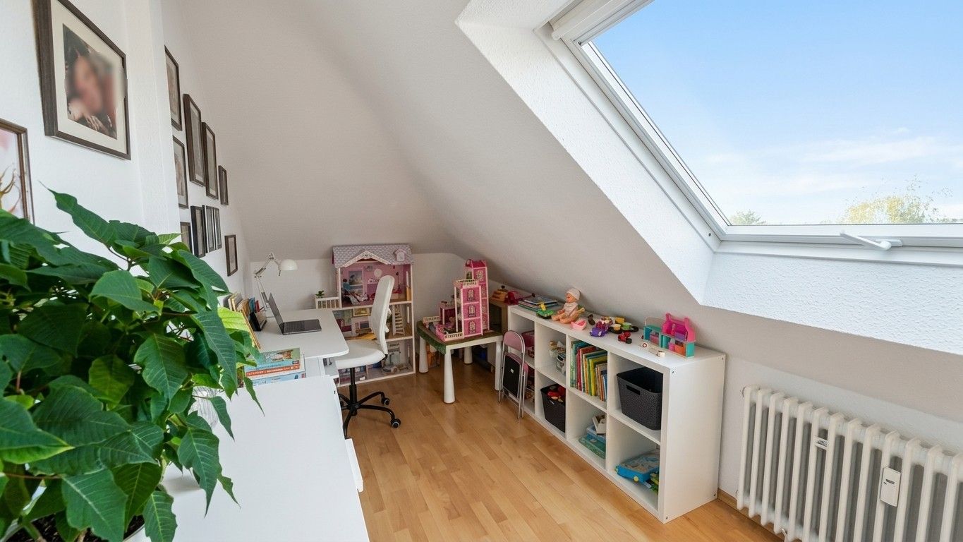 Helles Kinderzimmer mit Schreibtisch, Spielzeugregal und großem Dachfenster.