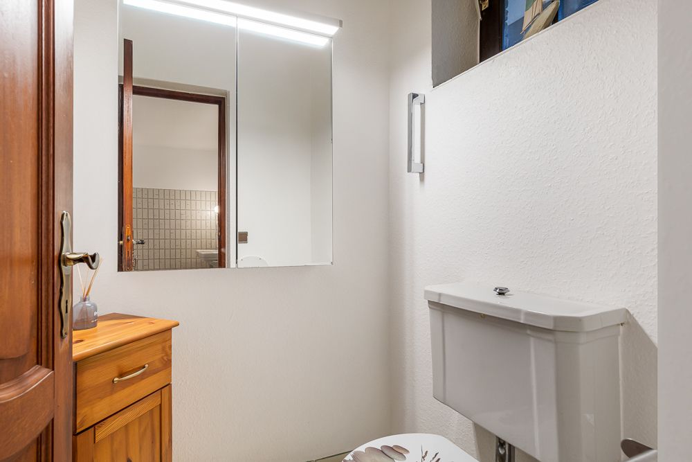 Kleines Badezimmer mit Holzschrank, Spiegel und Toilette.