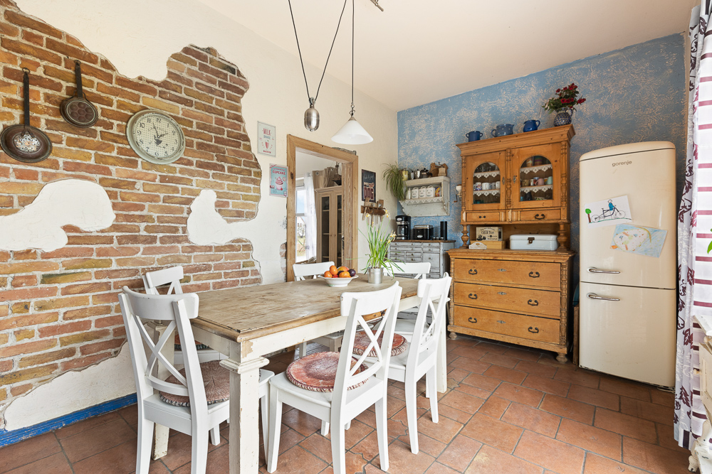 Gemütliche Küche mit Holztisch, weißen Stühlen, Backsteinwand, Vintage-Kühlschrank und Holzschrank.