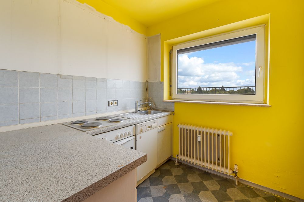 Kleine Küche mit gelben Wänden, Herd, Spüle, Heizung und Fenster mit Blick nach draußen.