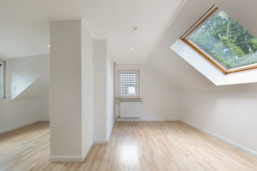Heller Raum mit Dachfenster, weiß gestrichenen Wänden und hellem Holzboden.