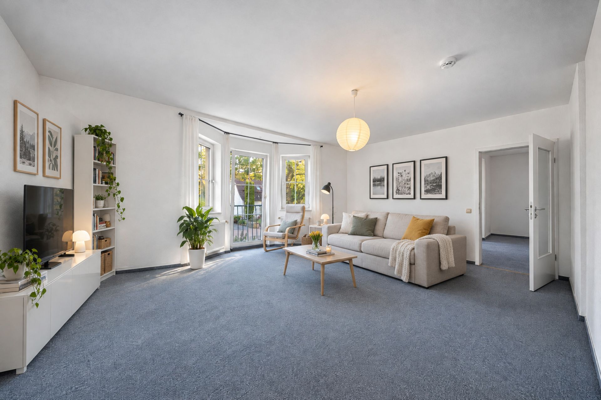 Helles Wohnzimmer mit Sofa, Couchtisch, Fernseher, Pflanzen und großem Fenster zum Balkon.