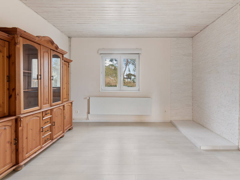 Helles Wohnzimmer mit Holzschrank, Fenster, Heizung und heller Bodenfliese.