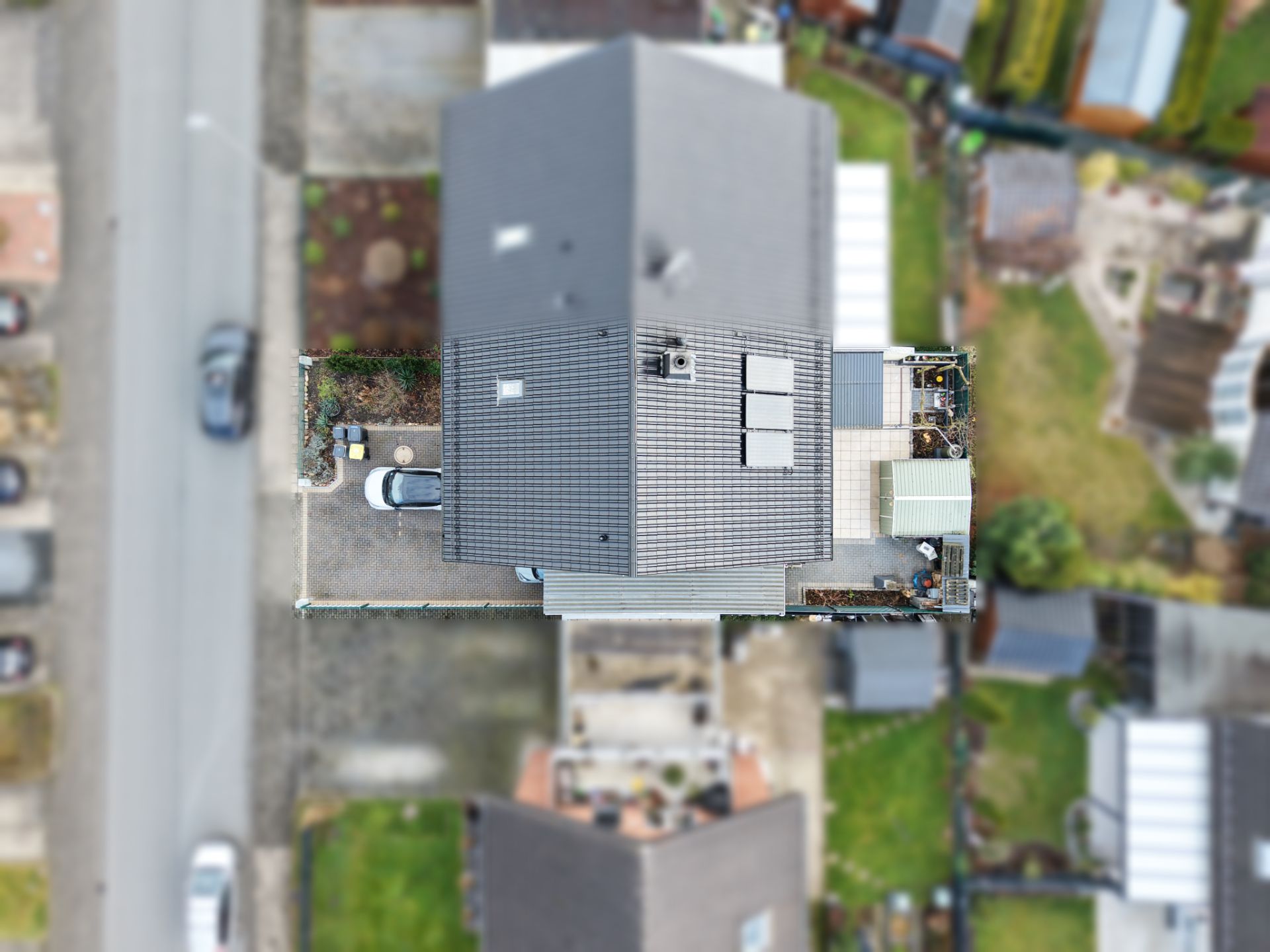 Luftaufnahme eines Einfamilienhauses mit grauem Dach und kleinem Hof, daneben eine Straße.