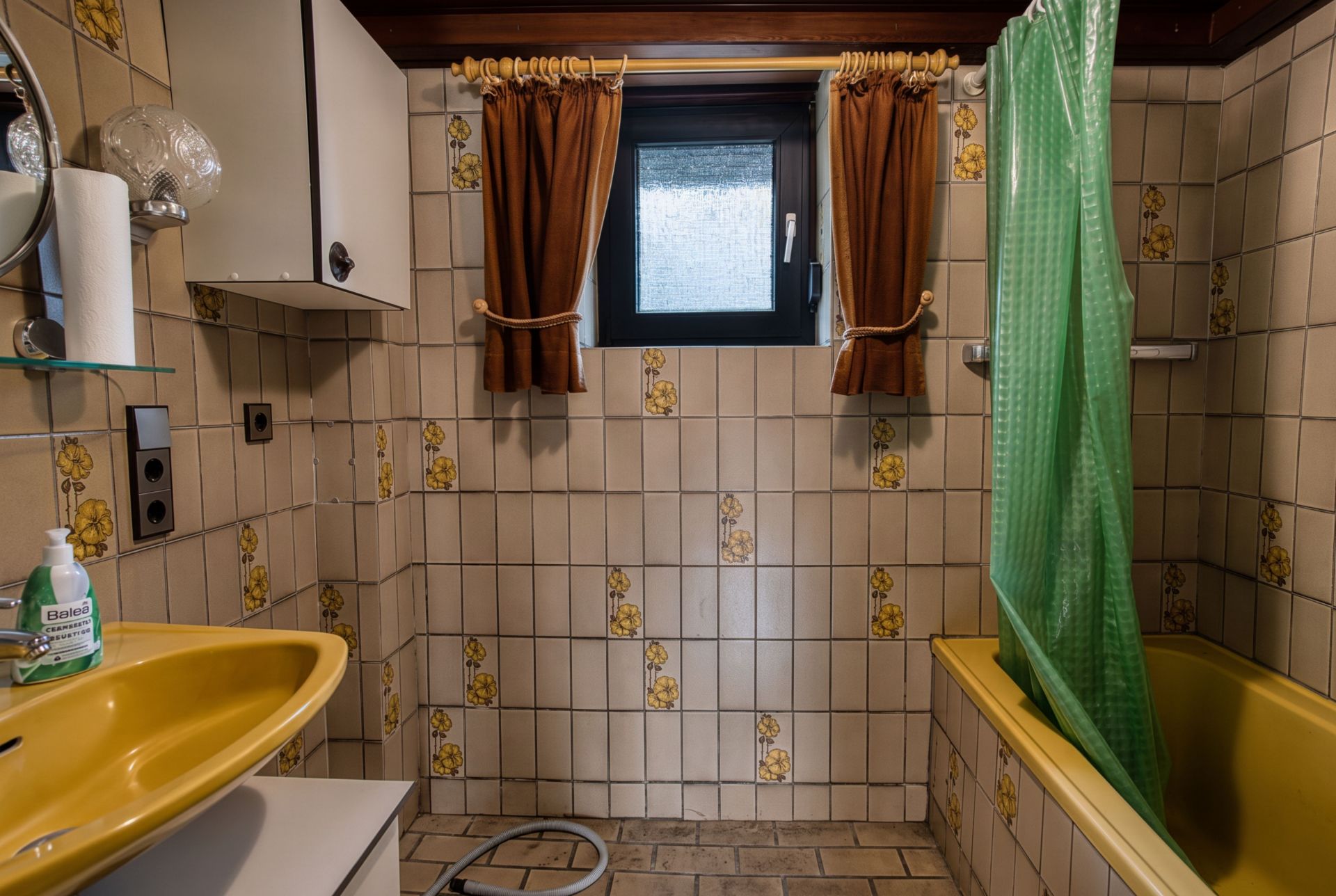 Badezimmer mit gelbem Waschbecken, Badewanne und Vorhängen an einem kleinen Fenster.