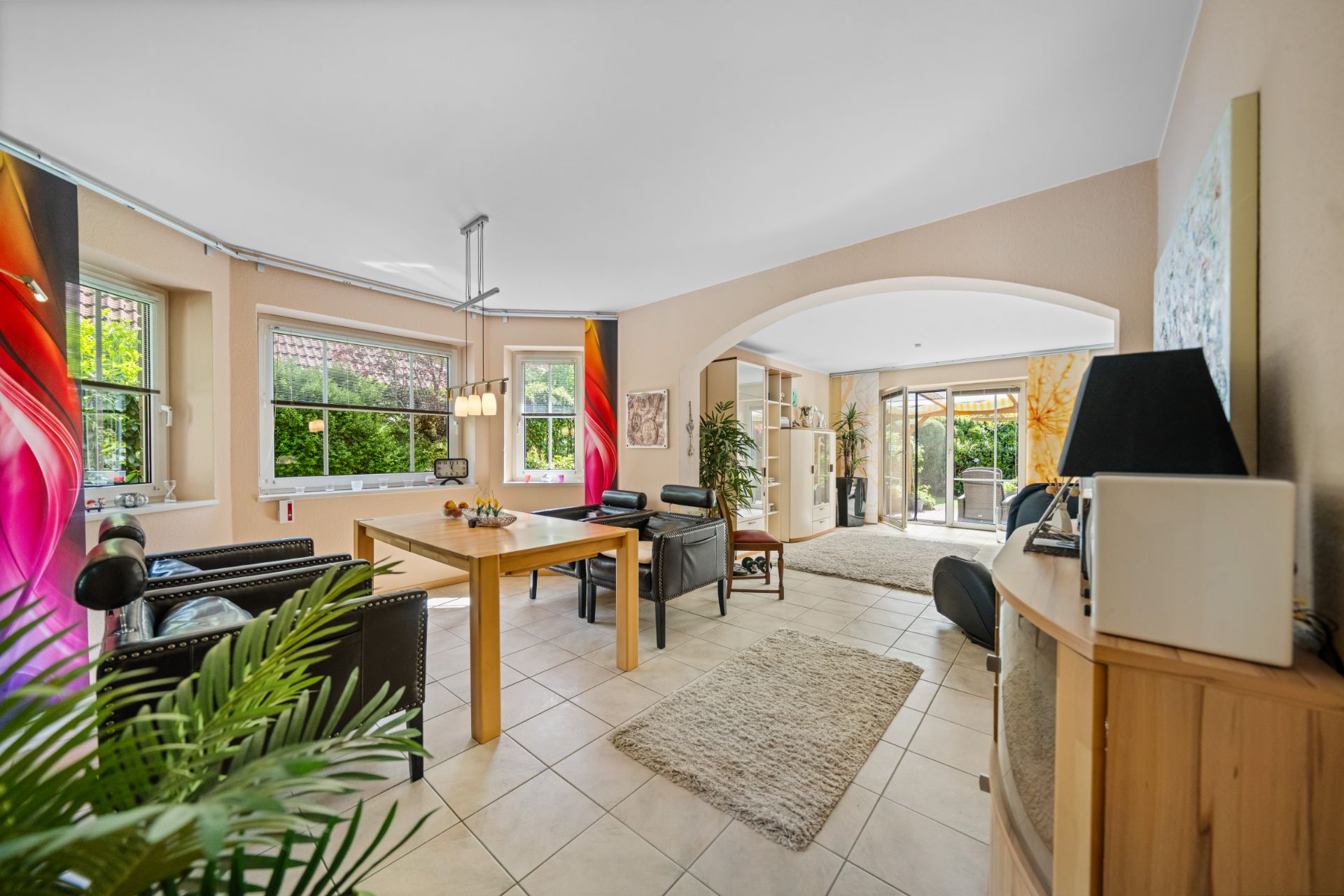 Helles Wohnzimmer mit Esstisch, Sesseln, Sofas und großen Fenstern, Zugang zur Terrasse.