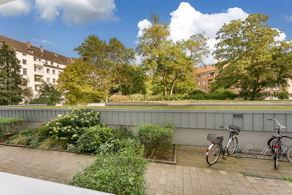 Blick auf einen Innenhof mit Grünpflanzen und geparkten Fahrrädern, dahinter Wohngebäude und Bäume.