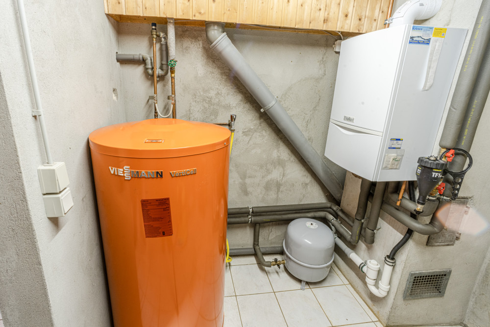 Heizungsraum mit orangefarbenem Warmwasserspeicher und weißer Heizungsanlage an der Wand.