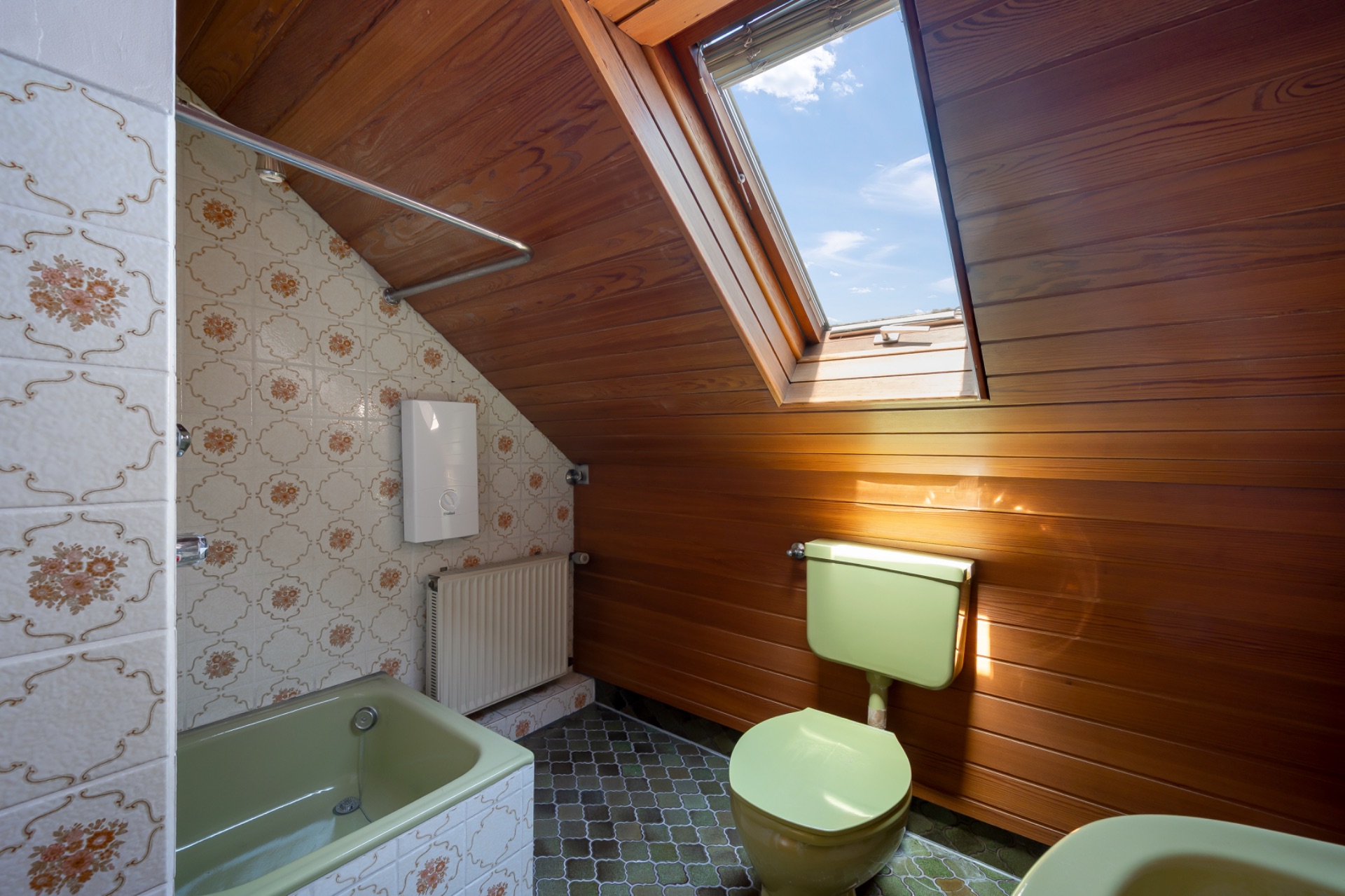 Badezimmer mit Badewanne, Toilette und Dachfenster in einem Raum mit Holzvertäfelung.
