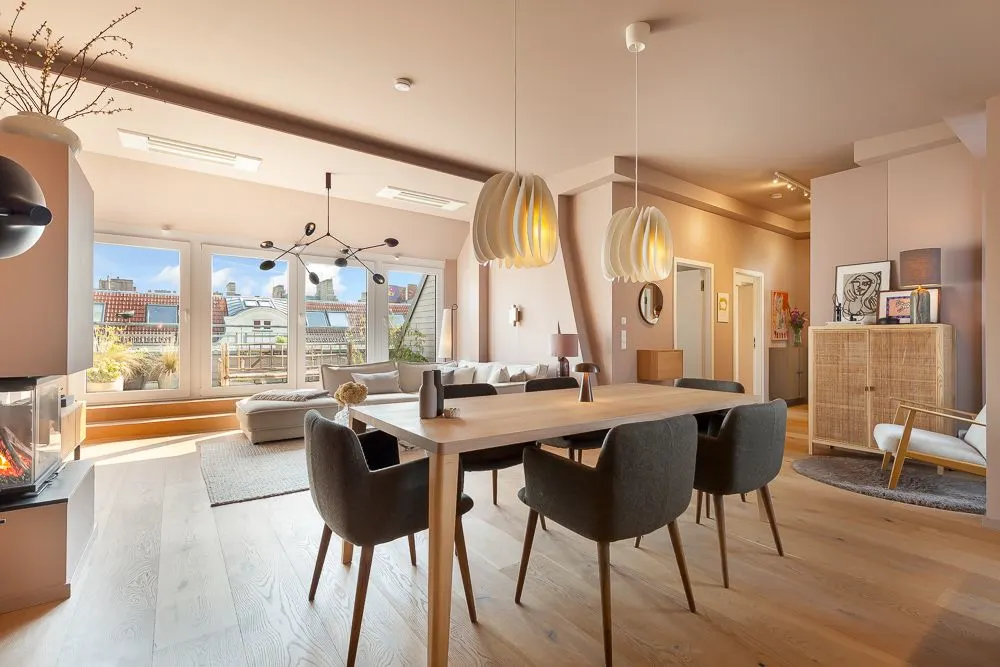 Helles Wohnzimmer mit Esstisch, Sesseln, Sofa, großen Fenstern und Kamin.