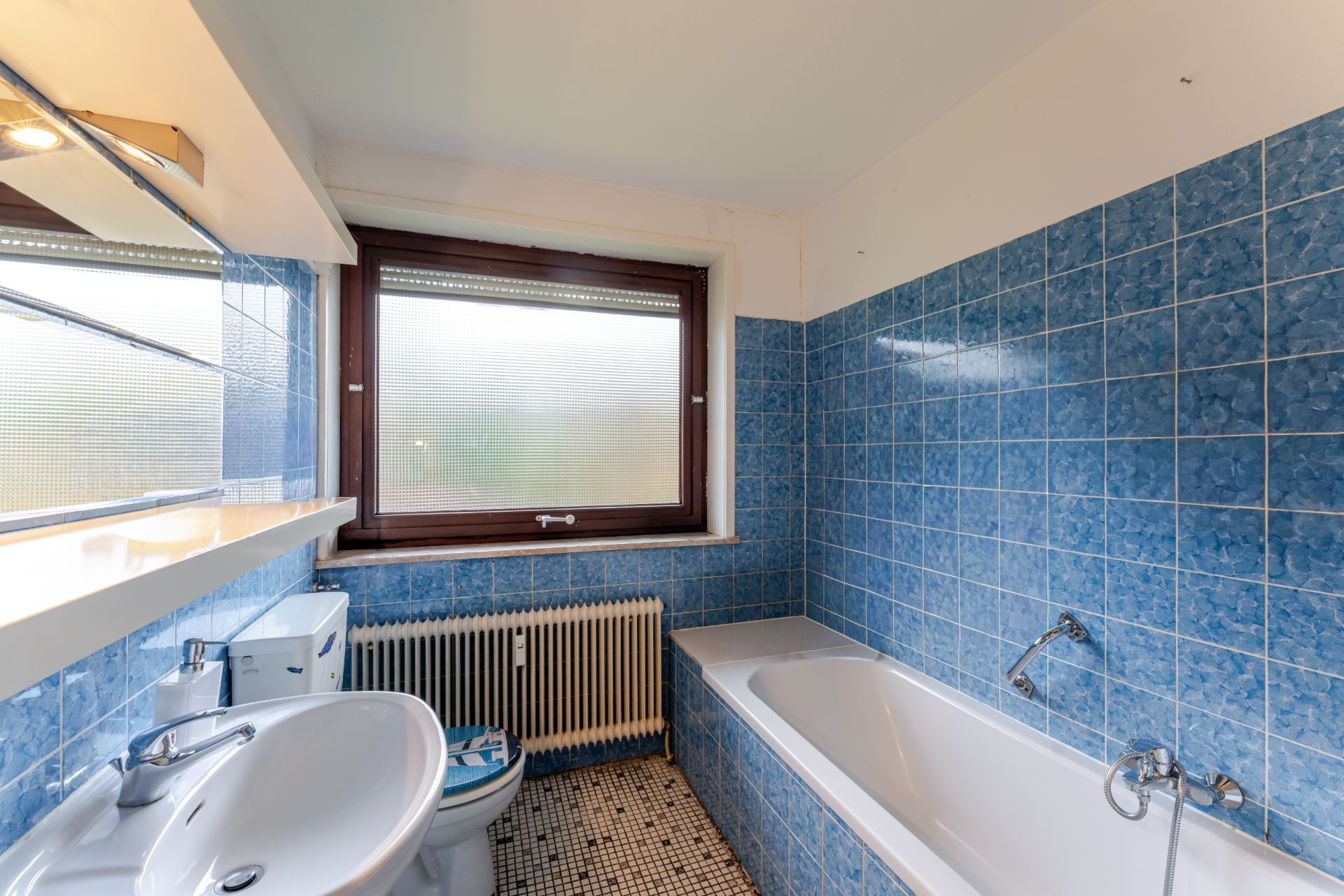 Badezimmer mit blauen Fliesen, Badewanne, Waschbecken, Toilette und großem Fenster.