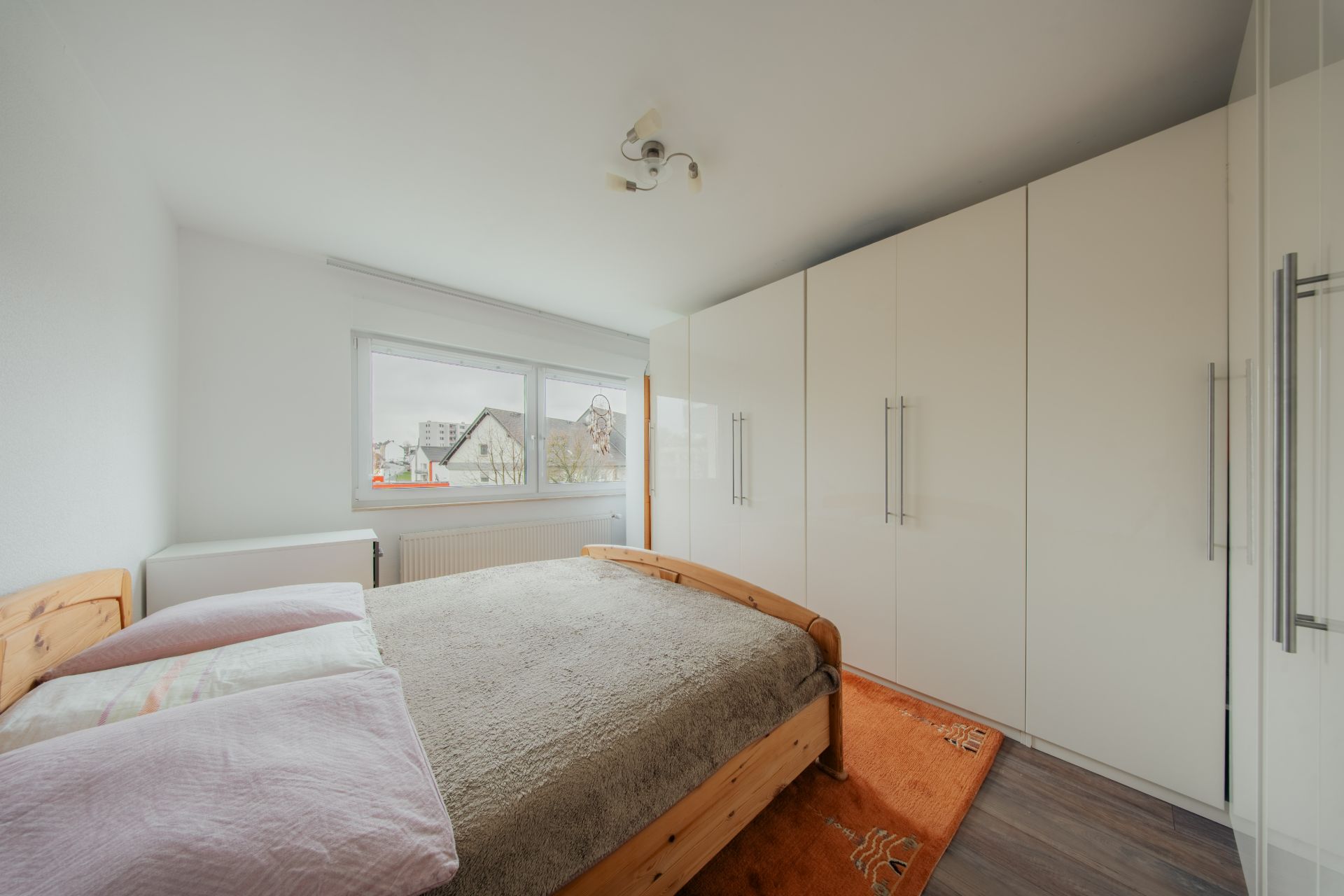 Schlafzimmer mit Doppelbett, großem weißen Kleiderschrank und Fenster mit Blick nach draußen.