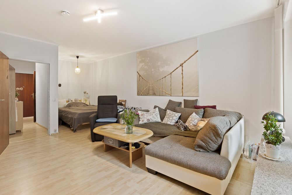 Wohnzimmer mit großer Eckcouch, Couchtisch, Pflanzen und offenem Blick ins Schlafzimmer.