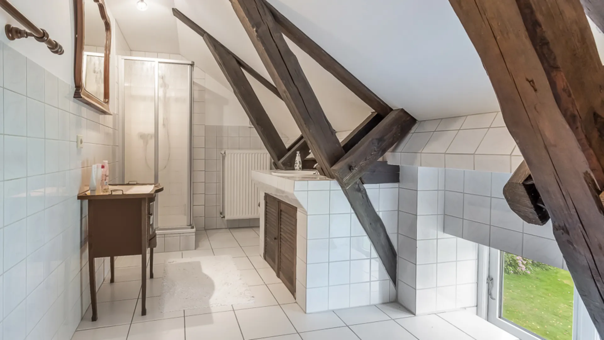 Helles Badezimmer mit Dusche, Waschbecken, schräger Decke und sichtbaren Holzbalken.