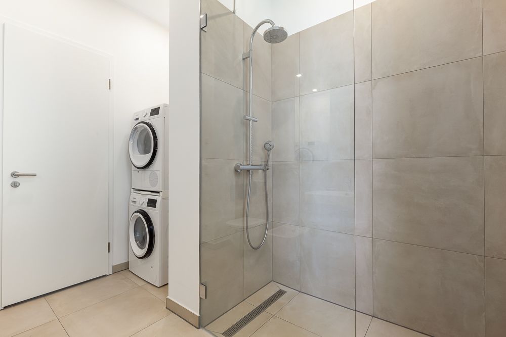 Modernes Badezimmer mit großer begehbarer Dusche und Waschmaschine mit Trockner.