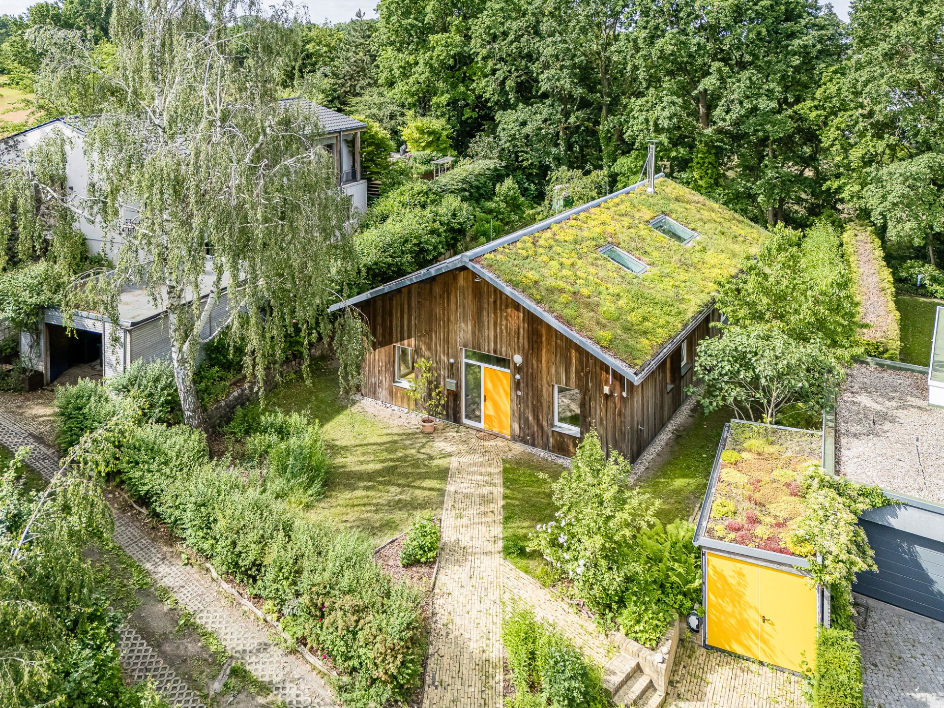 Modernes Holzhaus mit begrüntem Dach und gelber Tür, umgeben von Garten und Bäumen.