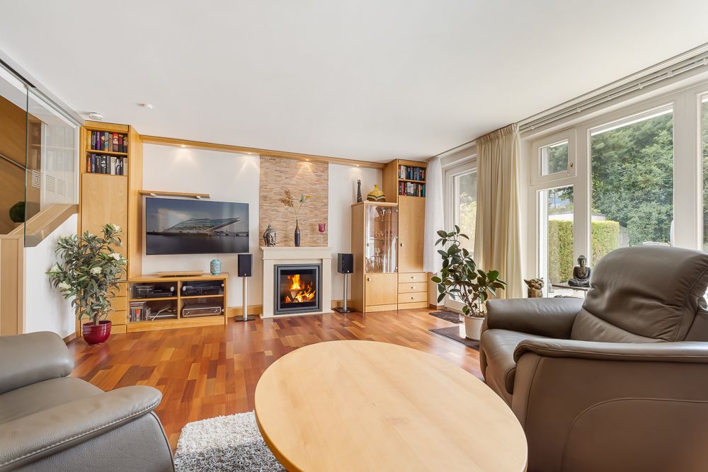 Helles Wohnzimmer mit Kamin, Ledersesseln, großem Fenster, Pflanzen und Holzmöbeln.