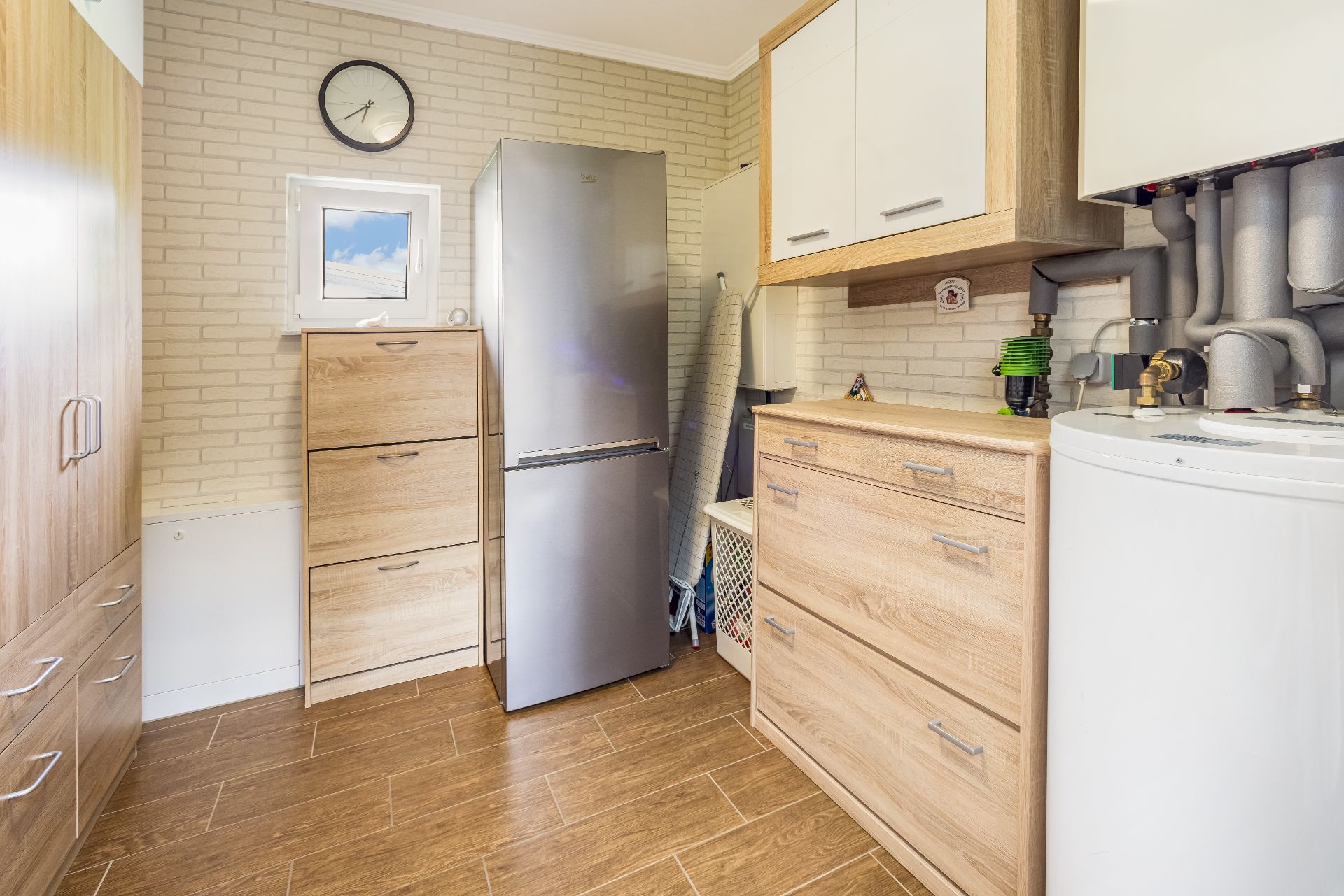 Hauswirtschaftsraum mit Holzschränken, Kühlschrank, Heizung, Fenster und Wanduhr.