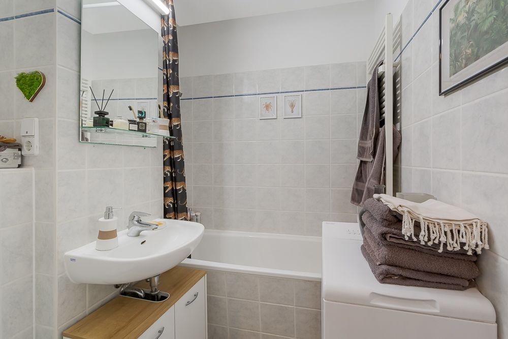 Kleines Badezimmer mit Waschbecken, Badewanne, Waschmaschine und gefalteten Handtüchern.