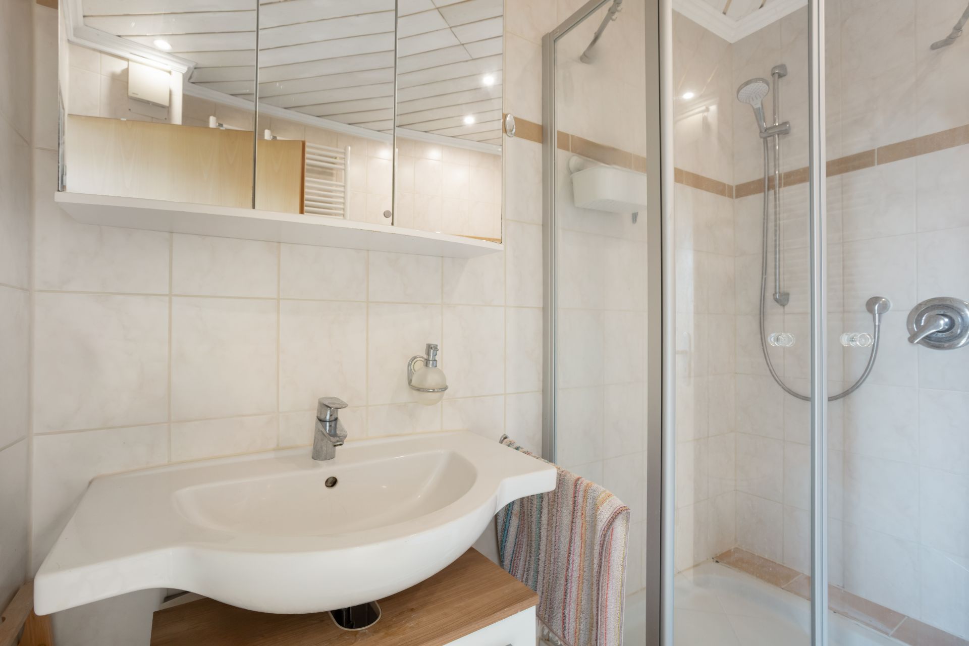 Helles Badezimmer mit Waschbecken, Spiegel, Dusche und Handtuch.
