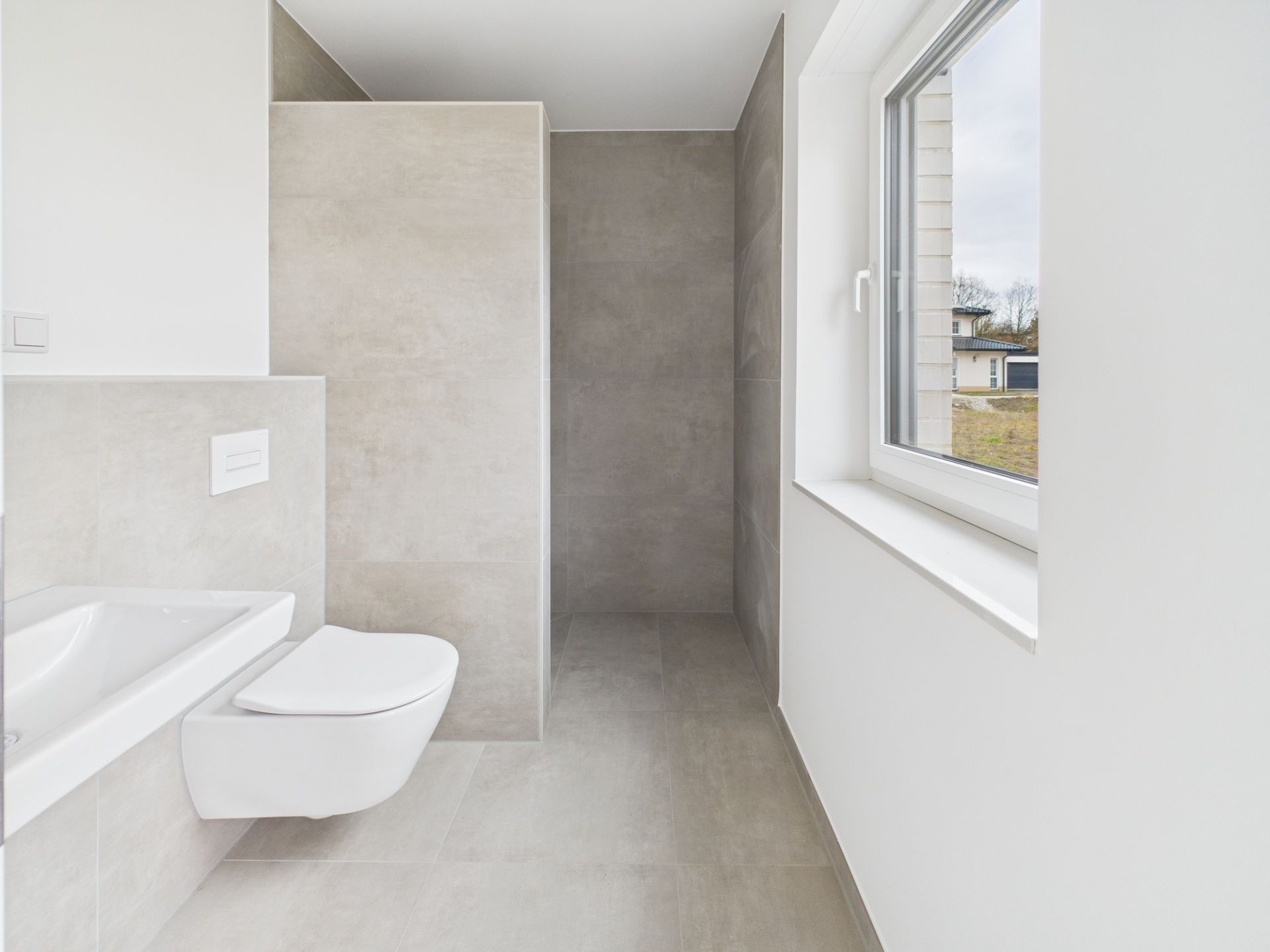 Modernes, helles Badezimmer mit bodengleicher Dusche, Wandtoilette und großem Fenster.