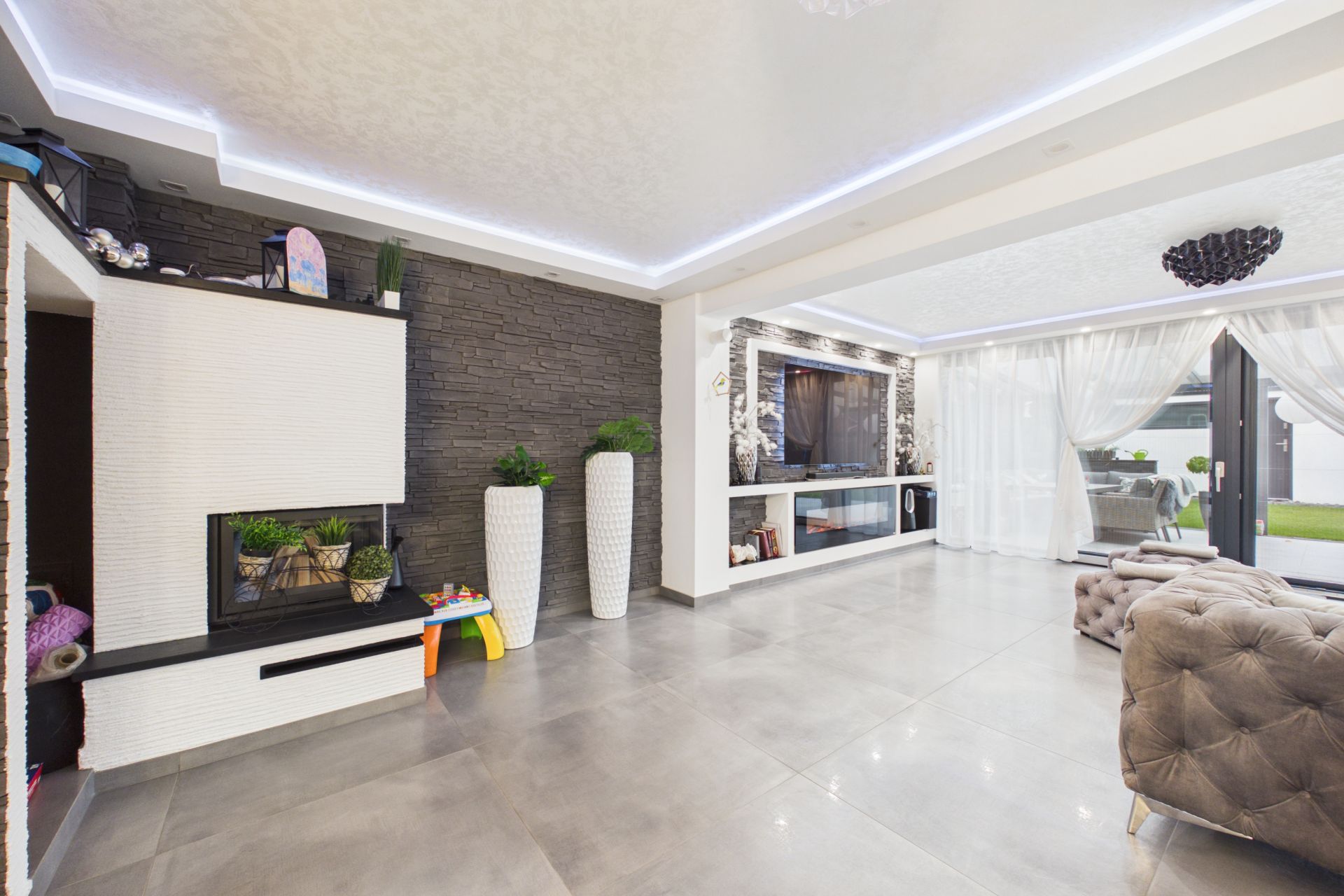 Modernes Wohnzimmer mit großen Fenstern, grauen Fliesen und weißen Dekorationselementen.