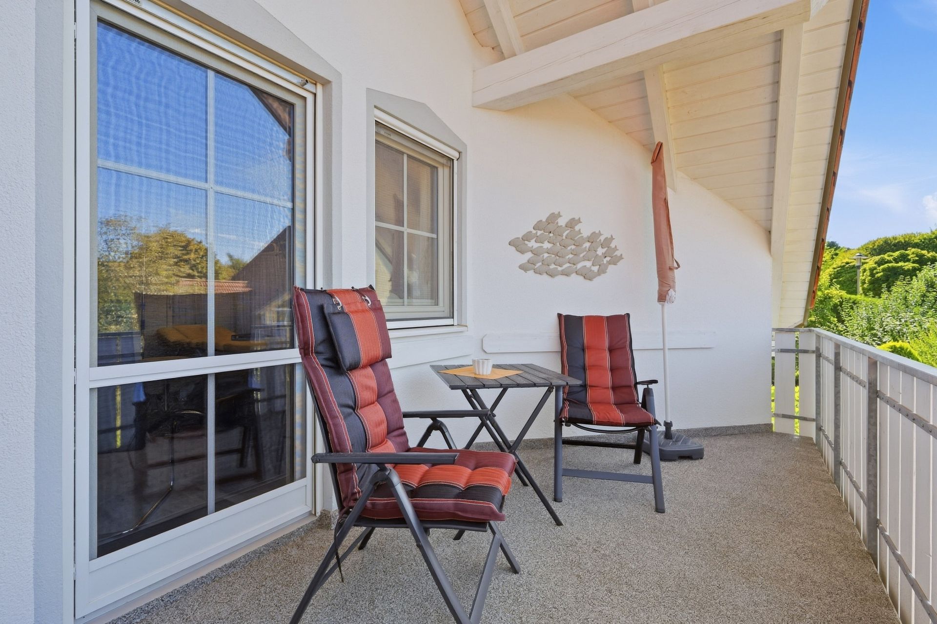 Balkon mit zwei gepolsterten Stühlen, Tisch und Wanddeko unter einem überdachten Dach.