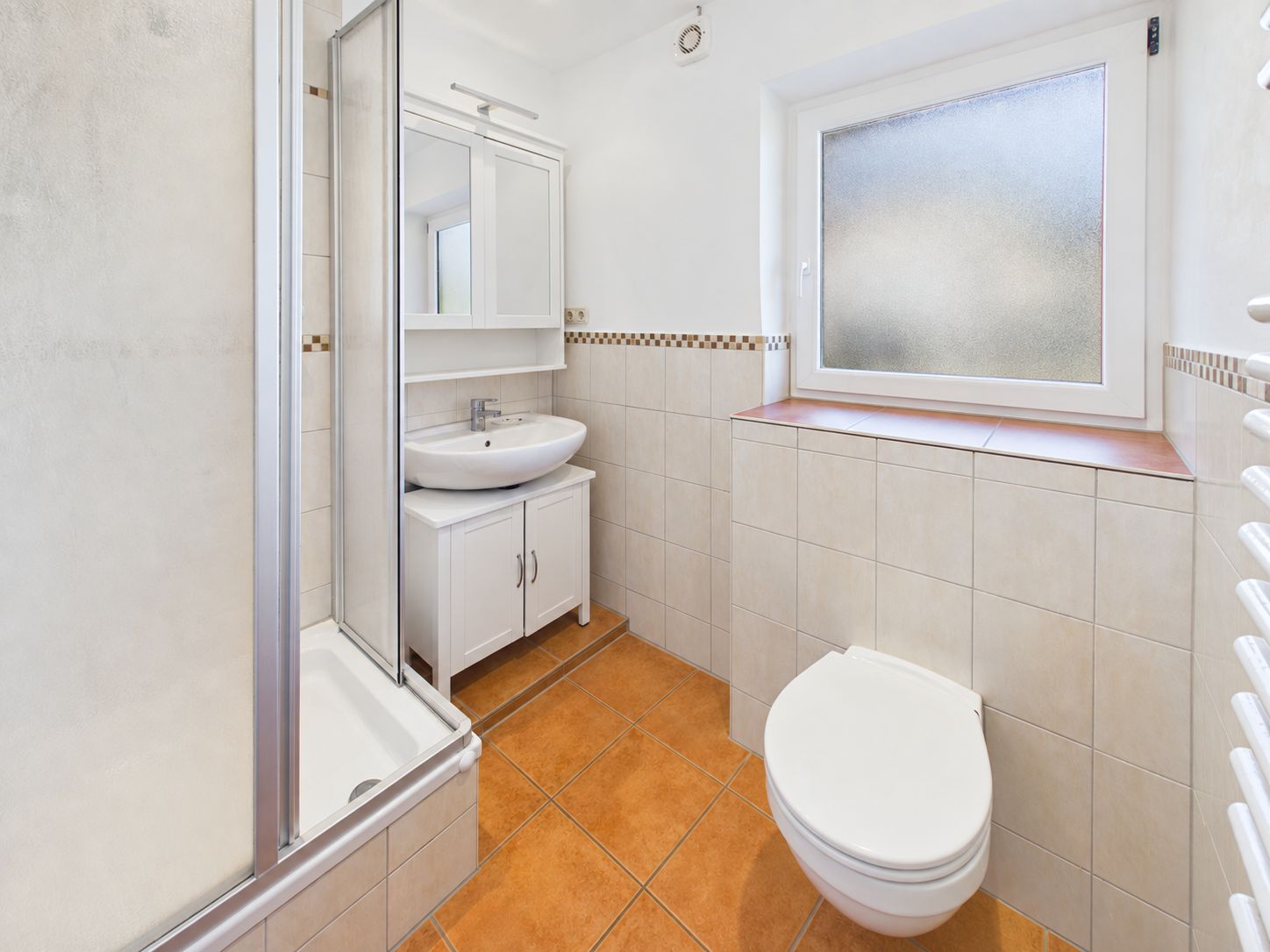 Helles Badezimmer mit Dusche, Waschbecken, Spiegel, Toilette und Fenster.