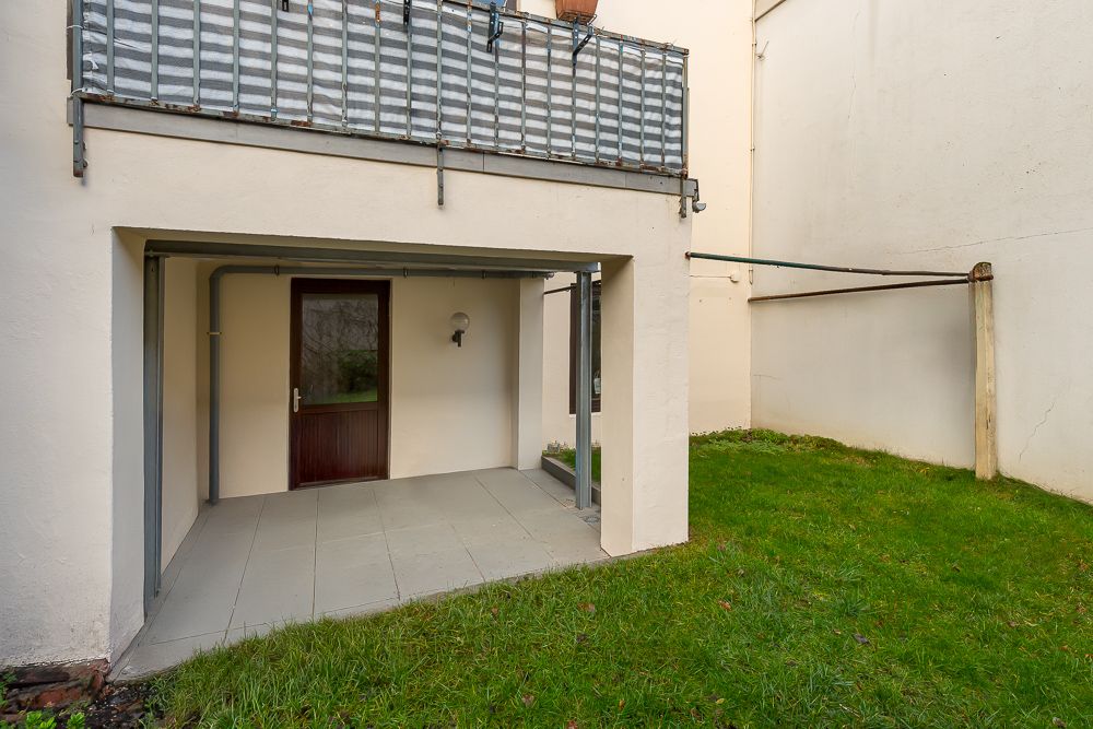 Überdachte Terrasse mit Fliesenboden und angrenzendem Grünfläche vor einer Tür.