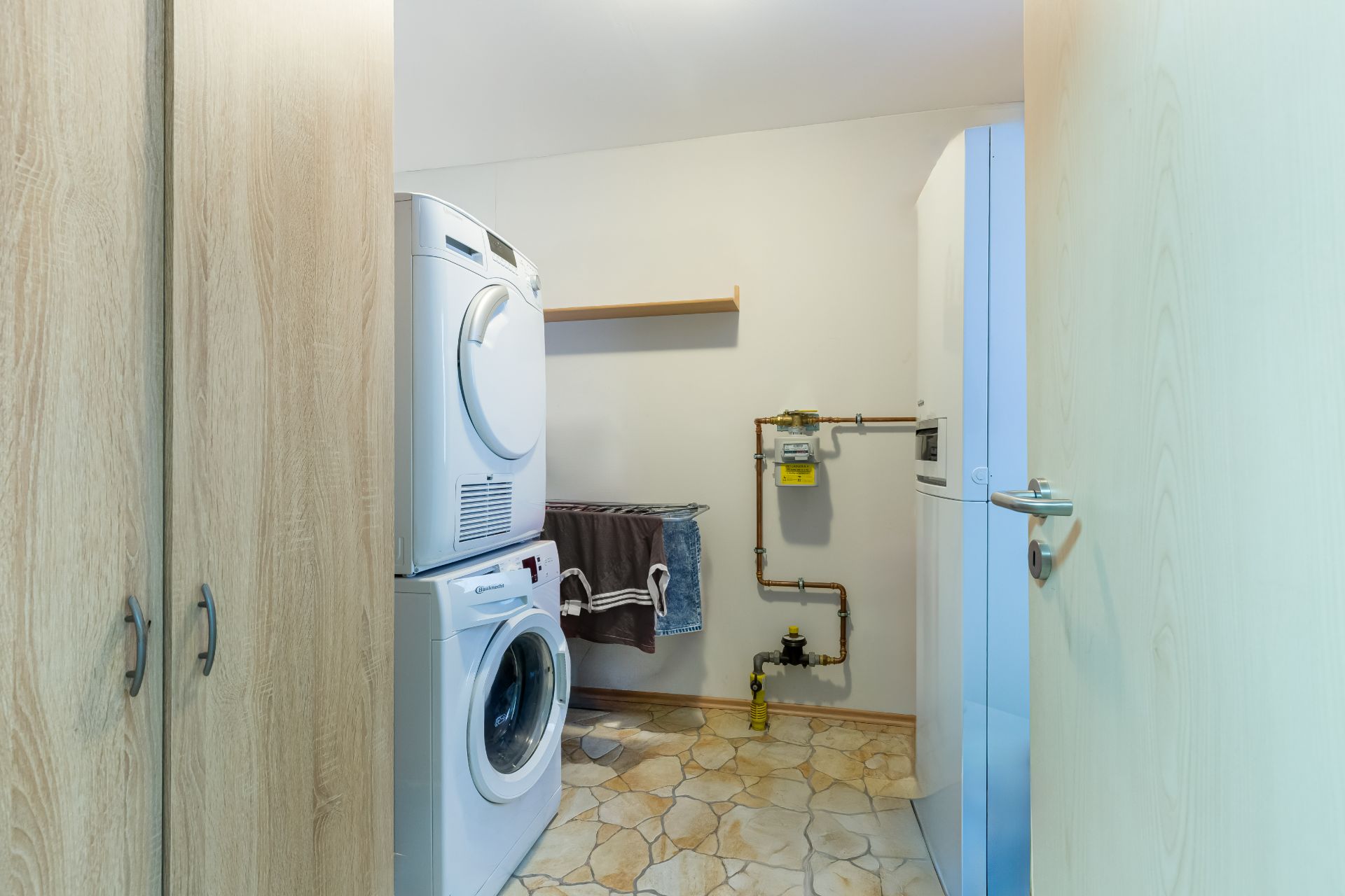 Waschküche mit Waschmaschine, Trockner, Schrank und offenem Regal.