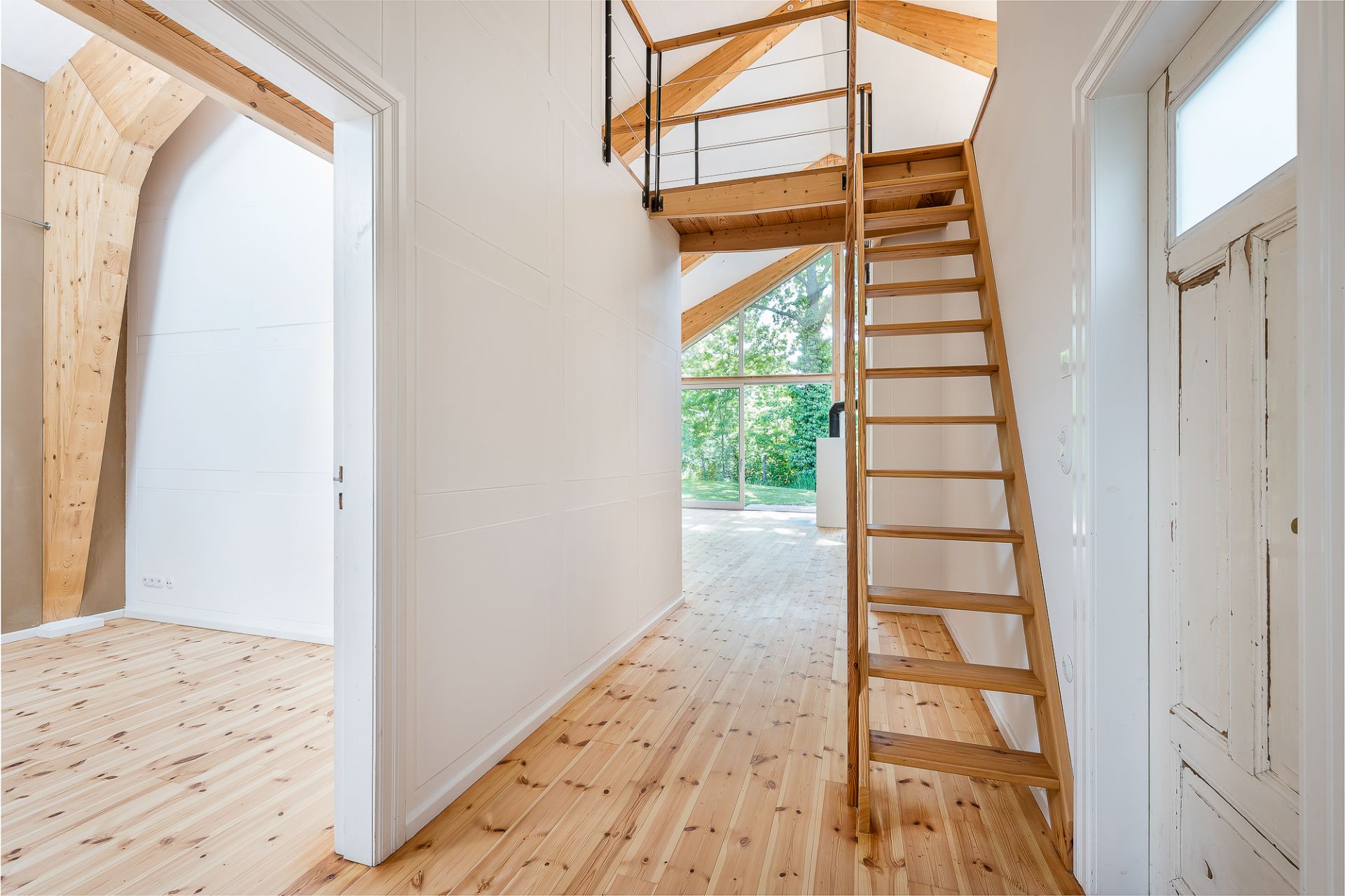Heller Flur mit Holztreppe, Holzboden und großer Fensterfront im Hintergrund.
