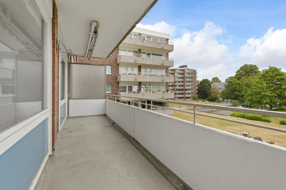 Großer Balkon mit Geländer, Blick auf andere Wohnhäuser und grüne Bäume.