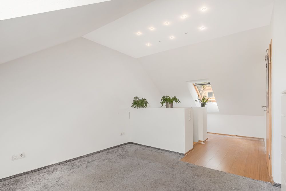 Heller Dachgeschossraum mit Teppichboden, Holzfußboden und drei Zimmerpflanzen auf einer weißen Brüstung.