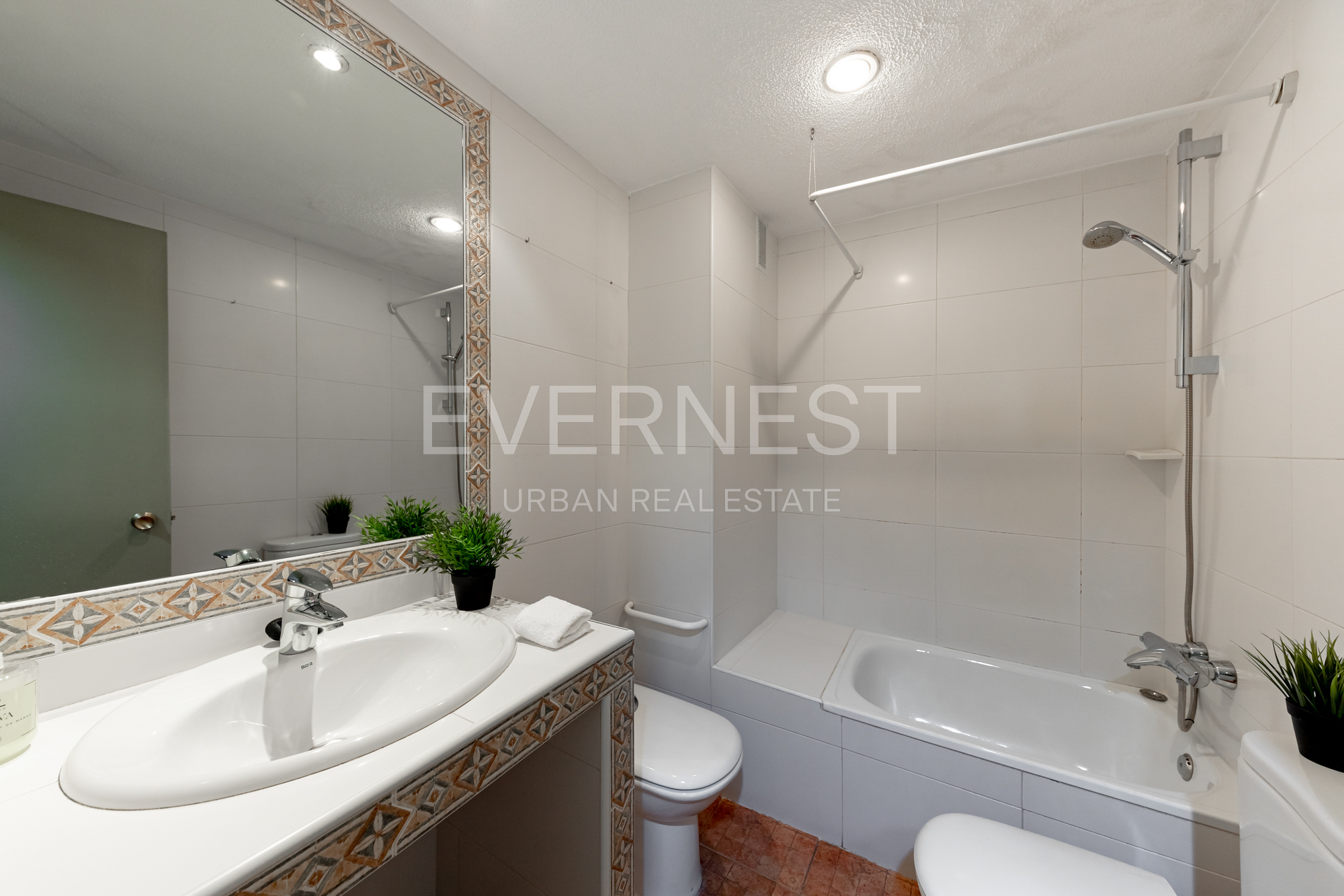 Helles Badezimmer mit Waschbecken, großem Spiegel, Toilette und Badewanne mit Dusche.