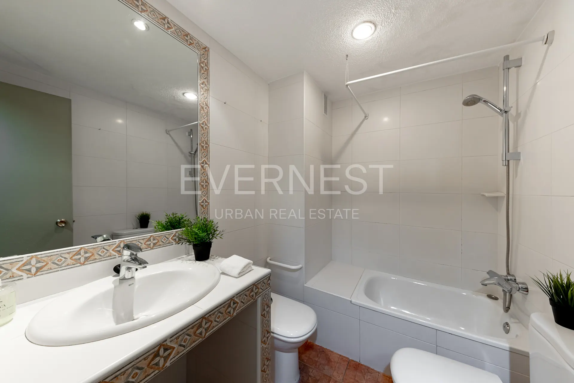 Helles Badezimmer mit Waschbecken, großem Spiegel, Toilette und Badewanne mit Dusche.