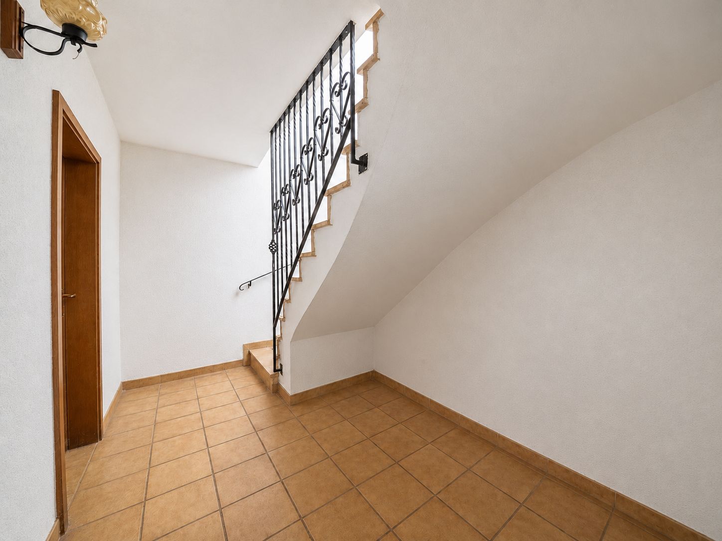 Heller Flur mit Fliesenboden, Treppe mit schwarzem Geländer und Holztür links.