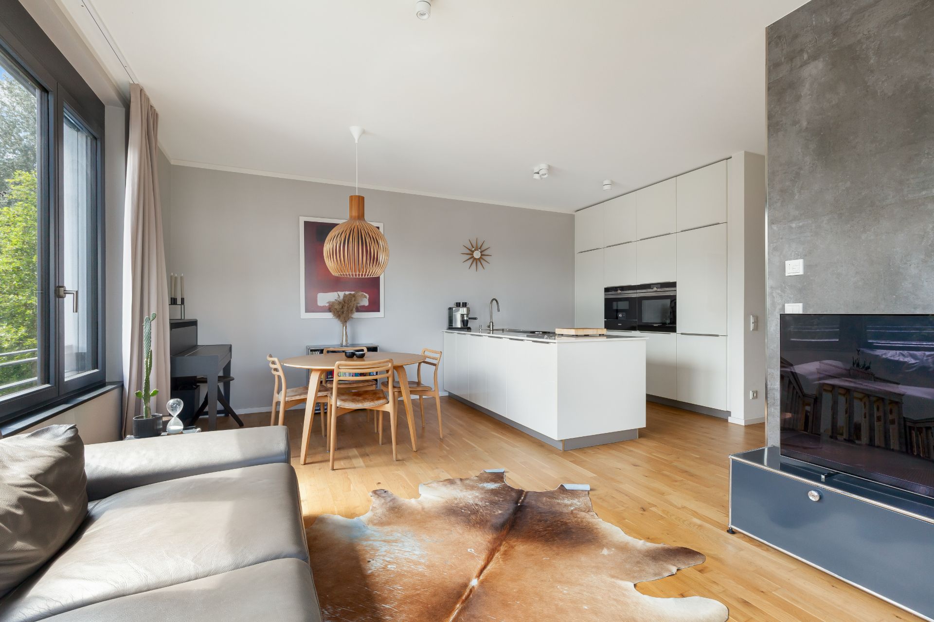 Helles Wohnzimmer mit offener Küche, Holzboden, Esstisch und Ledersofa.