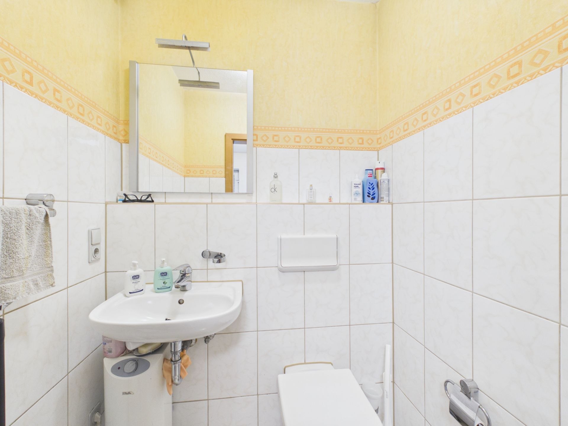 Kleines Badezimmer mit weiß gefliesten Wänden, Waschbecken, Spiegel und WC.