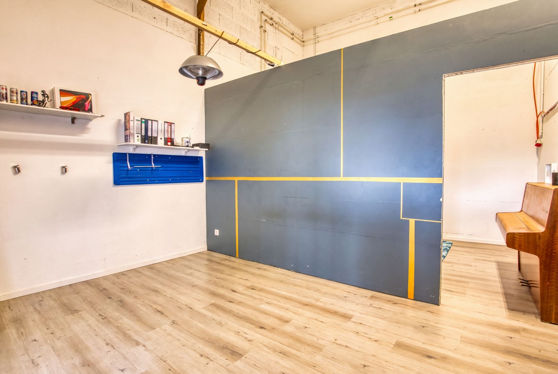 Heller Raum mit Holzboden, blauer Trennwand und Regal mit Ordnern an der weißen Wand.