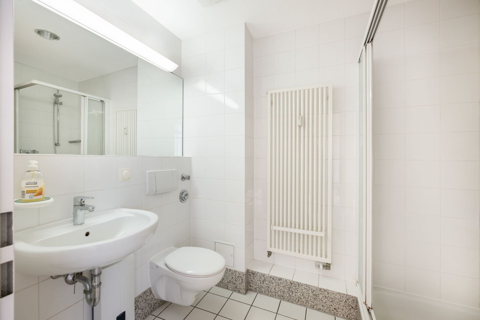 Helles Badezimmer mit Waschbecken, Spiegel, WC, Handtuchheizung und Dusche.