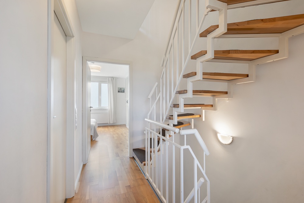 Heller Flur mit Holztreppe und Blick in ein Zimmer mit Fenster.