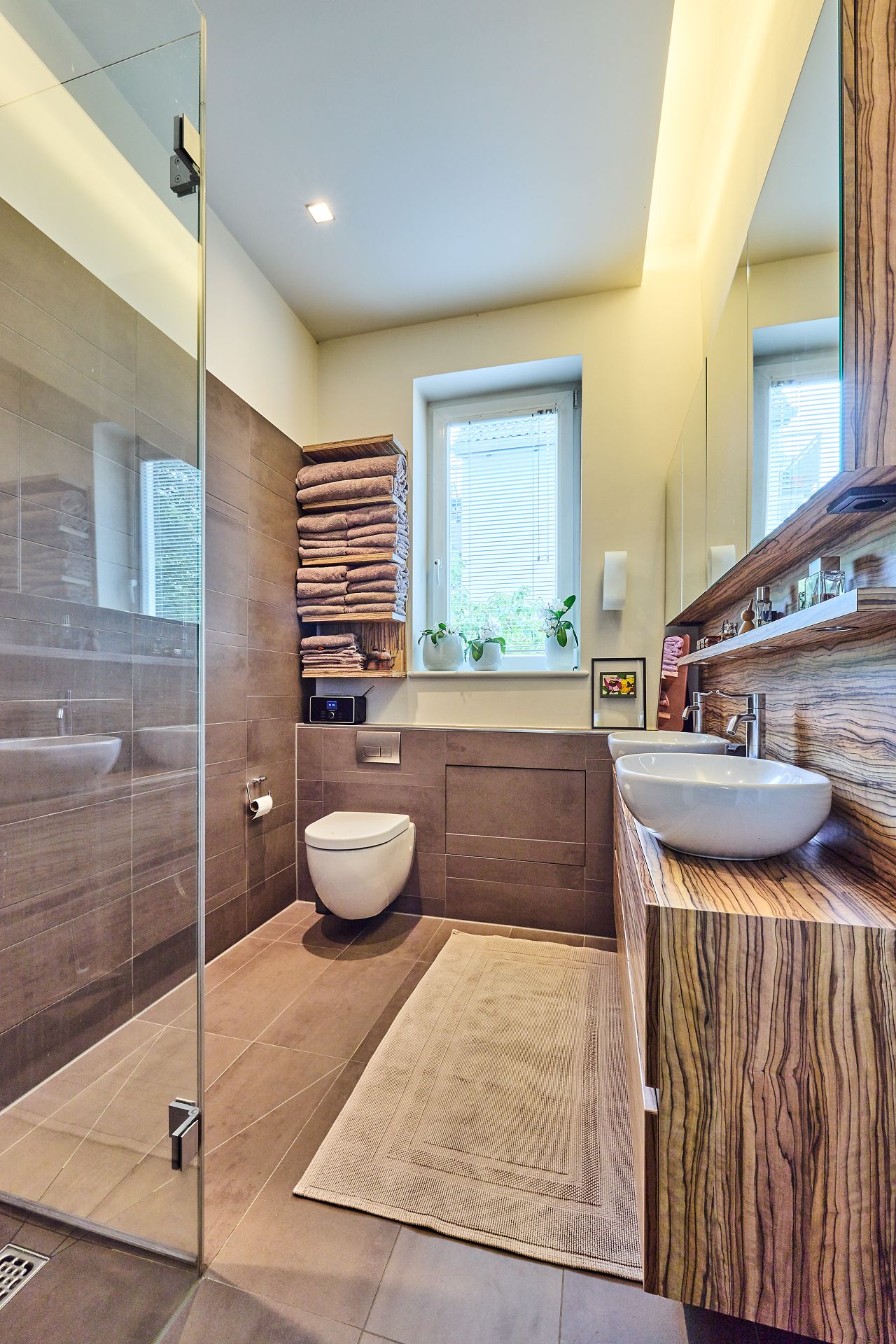 Modernes Badezimmer mit Dusche, Wandtoilette, Waschbecken und Fenster mit Pflanzen.