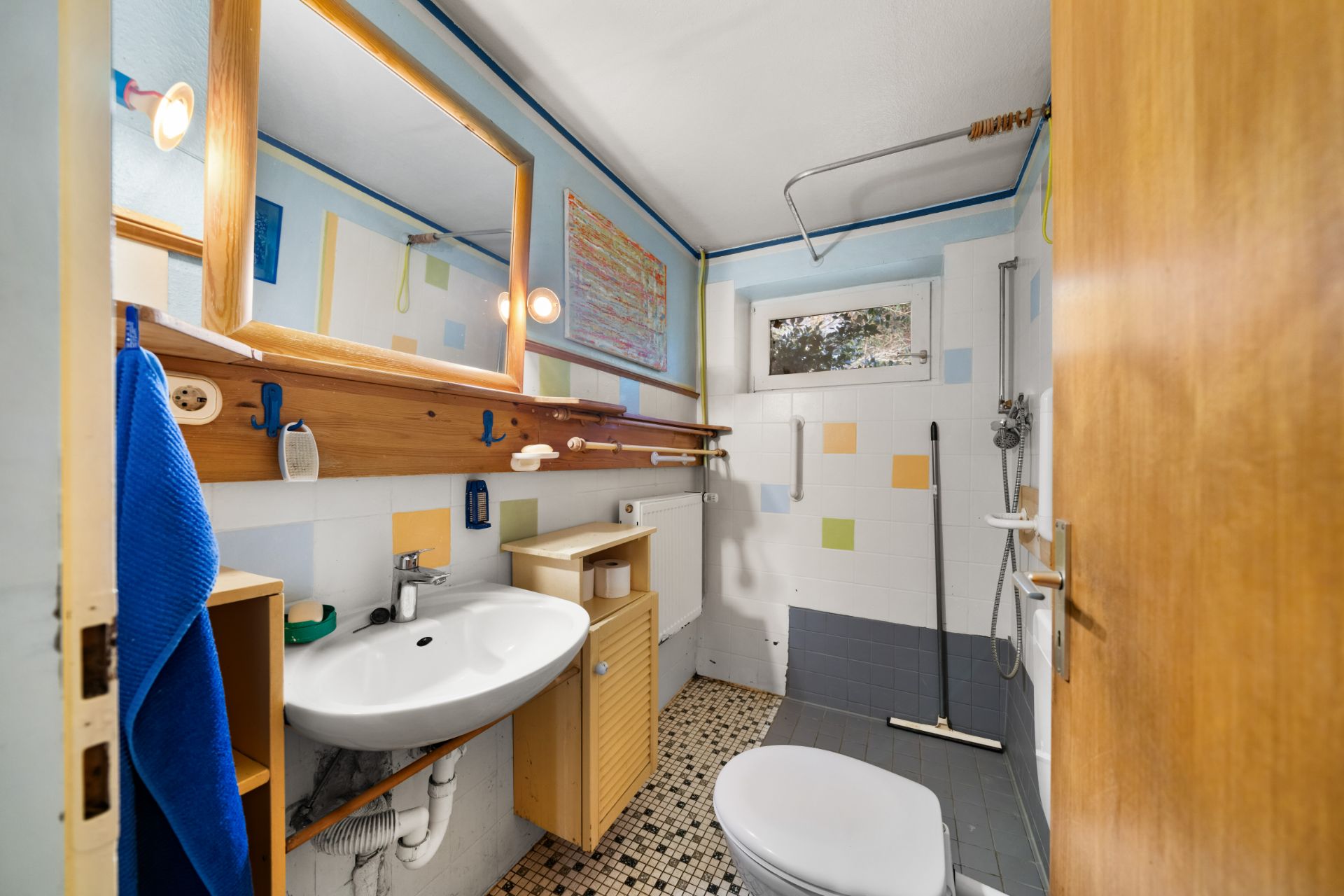 Kleines Badezimmer mit Waschbecken, Spiegel, Toilette, Dusche und bunten Fliesen.