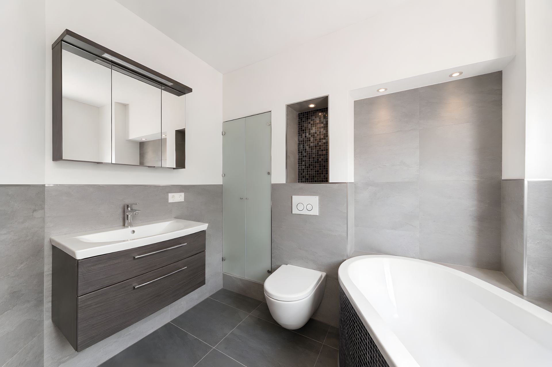 Modernes Badezimmer mit Badewanne, Toilette, Spiegel und Waschbecken mit Unterschrank.