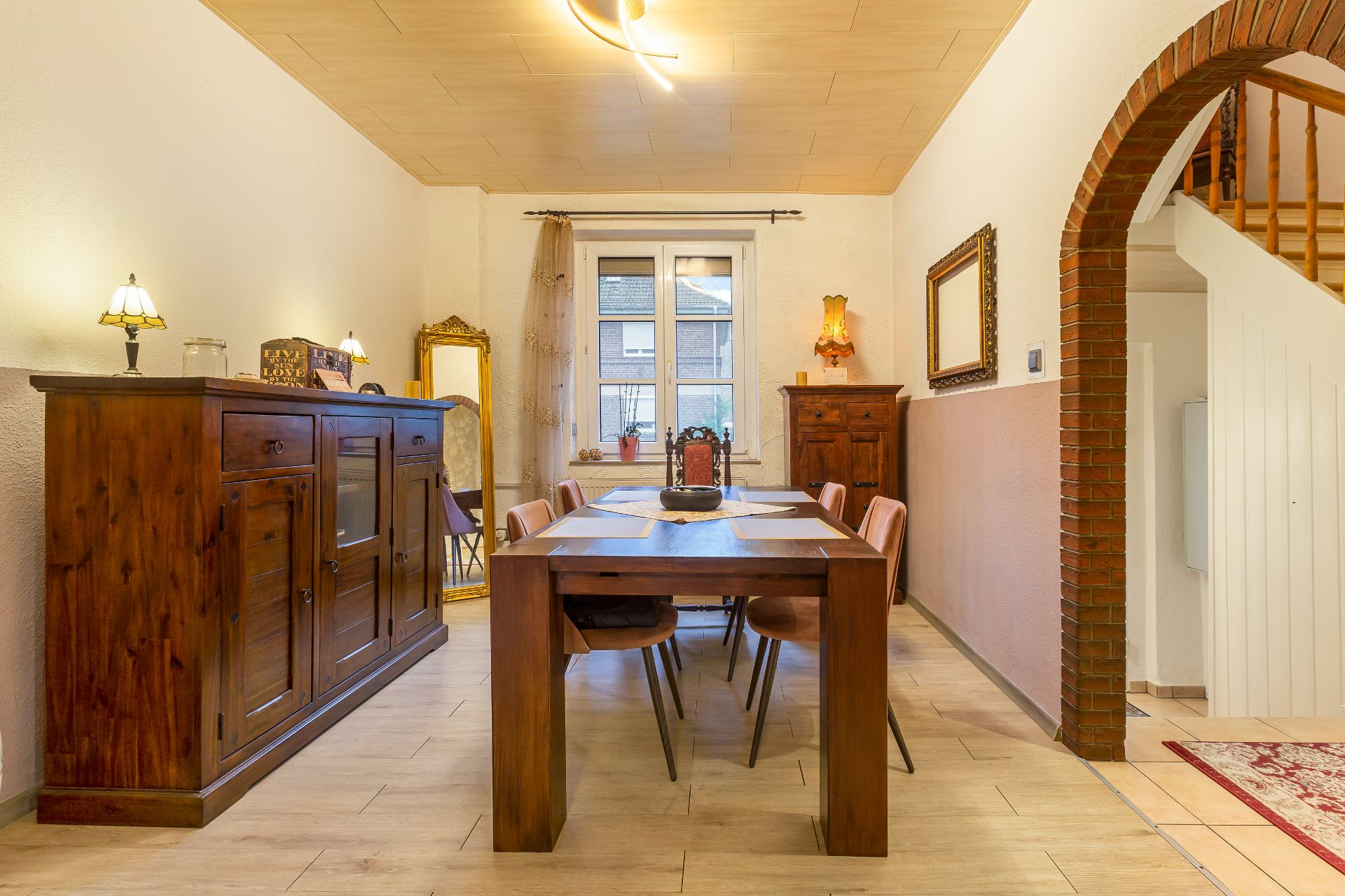Esszimmer mit Holztisch, sechs Stühlen, Kommode, Spiegel und Fenster in gemütlicher Einrichtung.