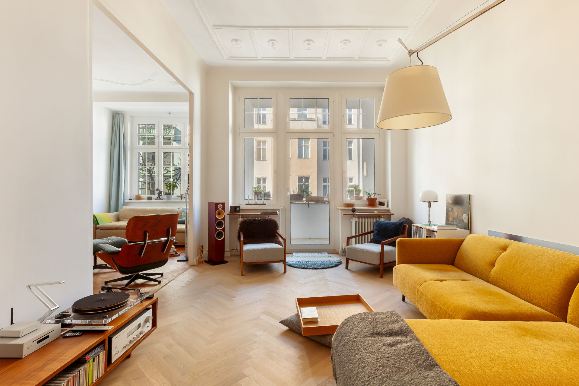 Helles Wohnzimmer mit gelbem Sofa, Sesseln, großen Fenstern und Holzboden.