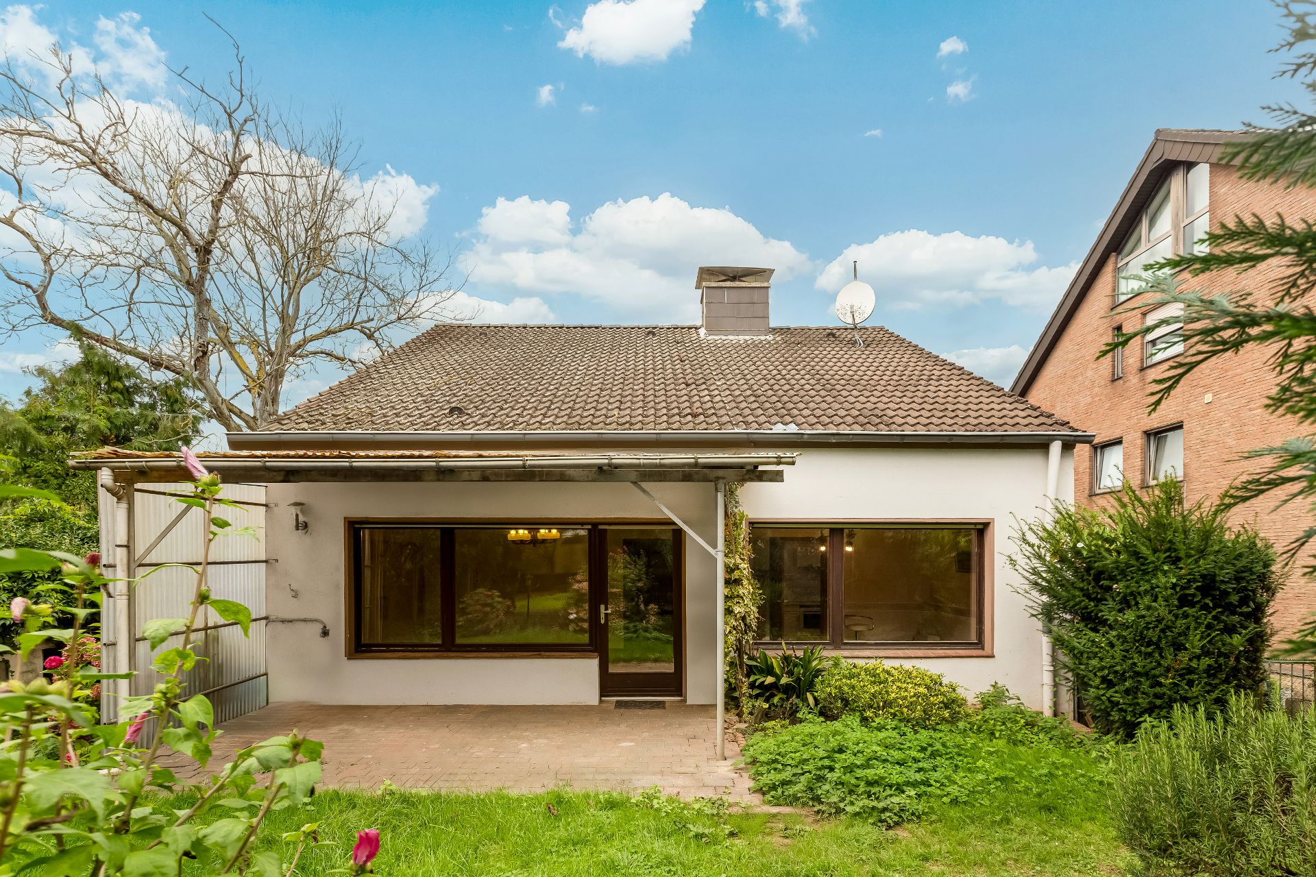 Einfamilienhaus mit großen Fenstern, Terrasse und Garten, neben anderen Häusern.